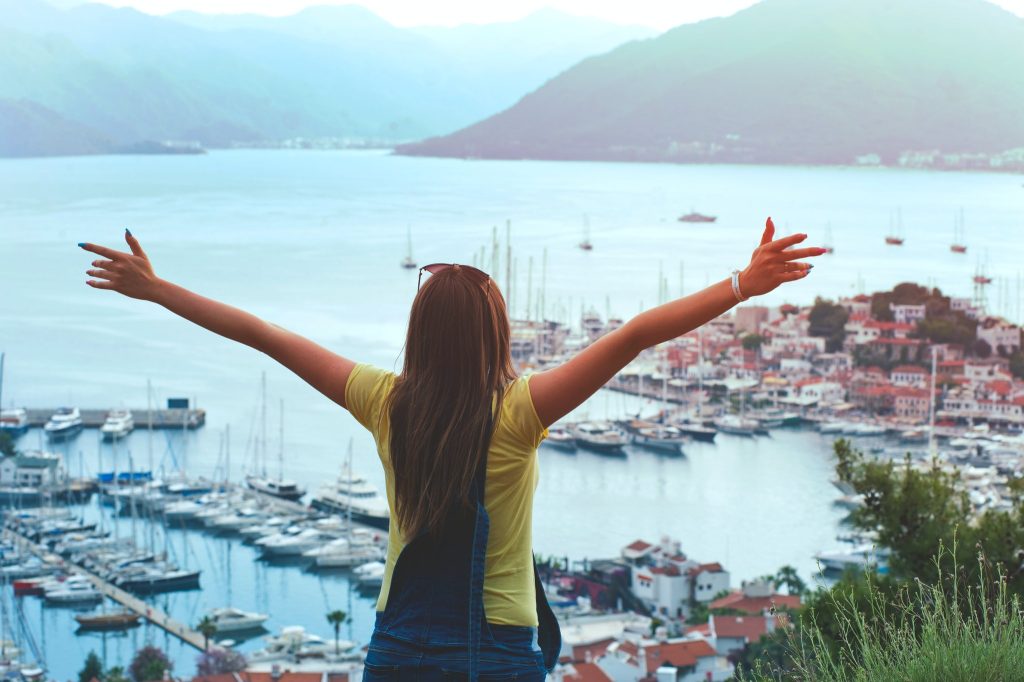 woman-raising-her-hands-facing-cityscape-near-body-of-water